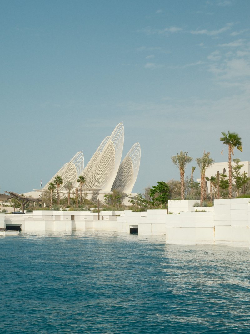 A modern architectural structure resembling petals near a calm blue water body under a clear sky.