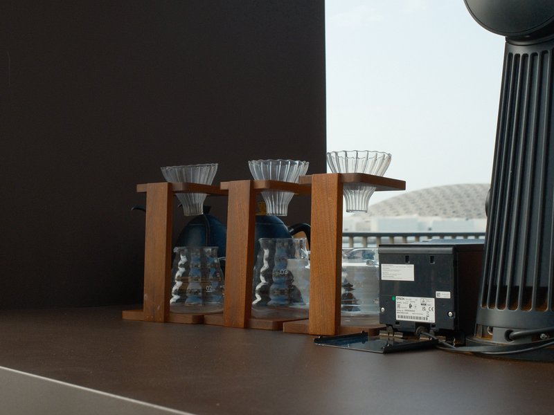 Three coffee brewing devices on a wooden table with a blurred background of a stadium.