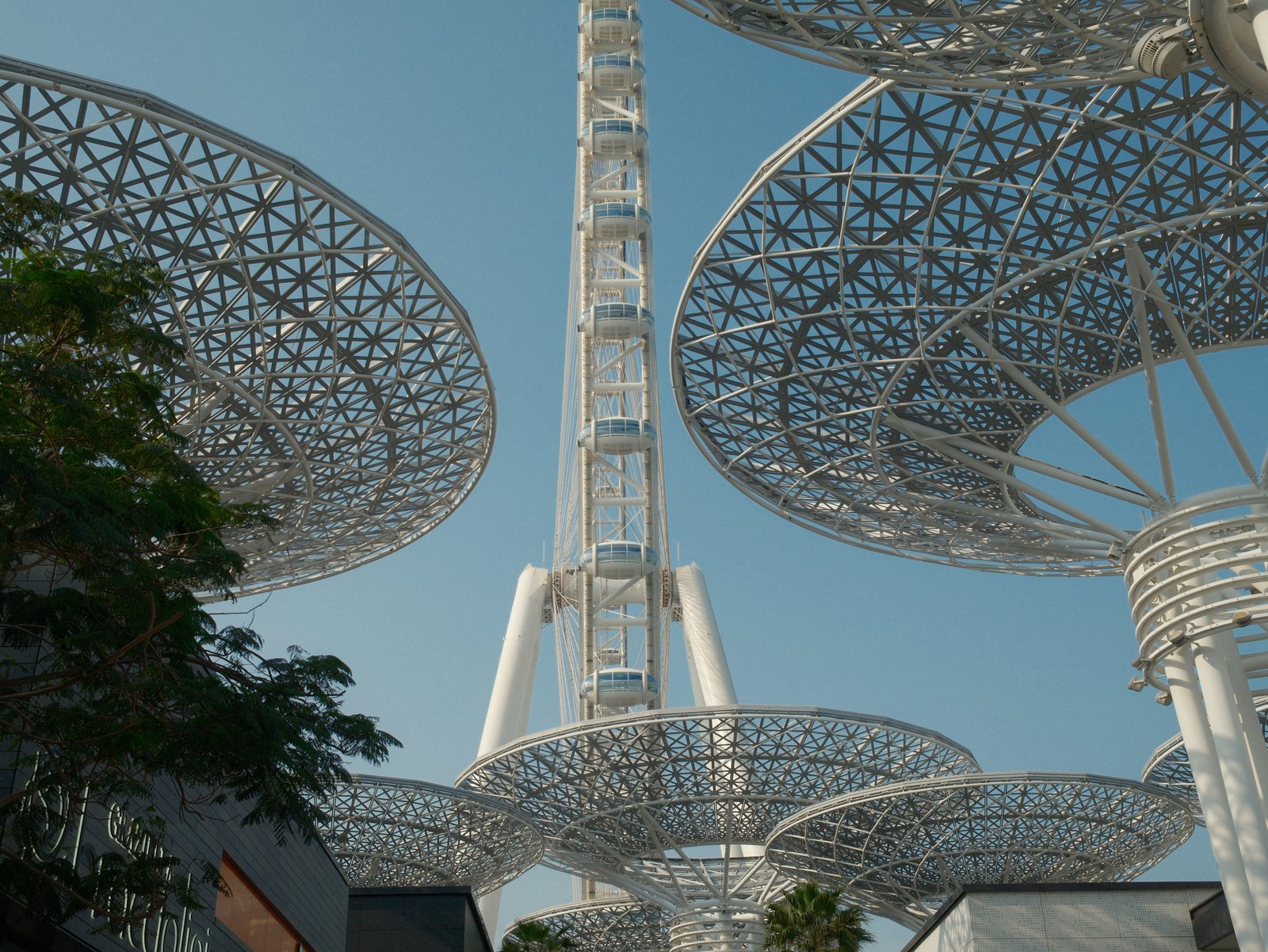 A modern architectural structure with large, circular canopies and a tall tower against a clear blue sky.