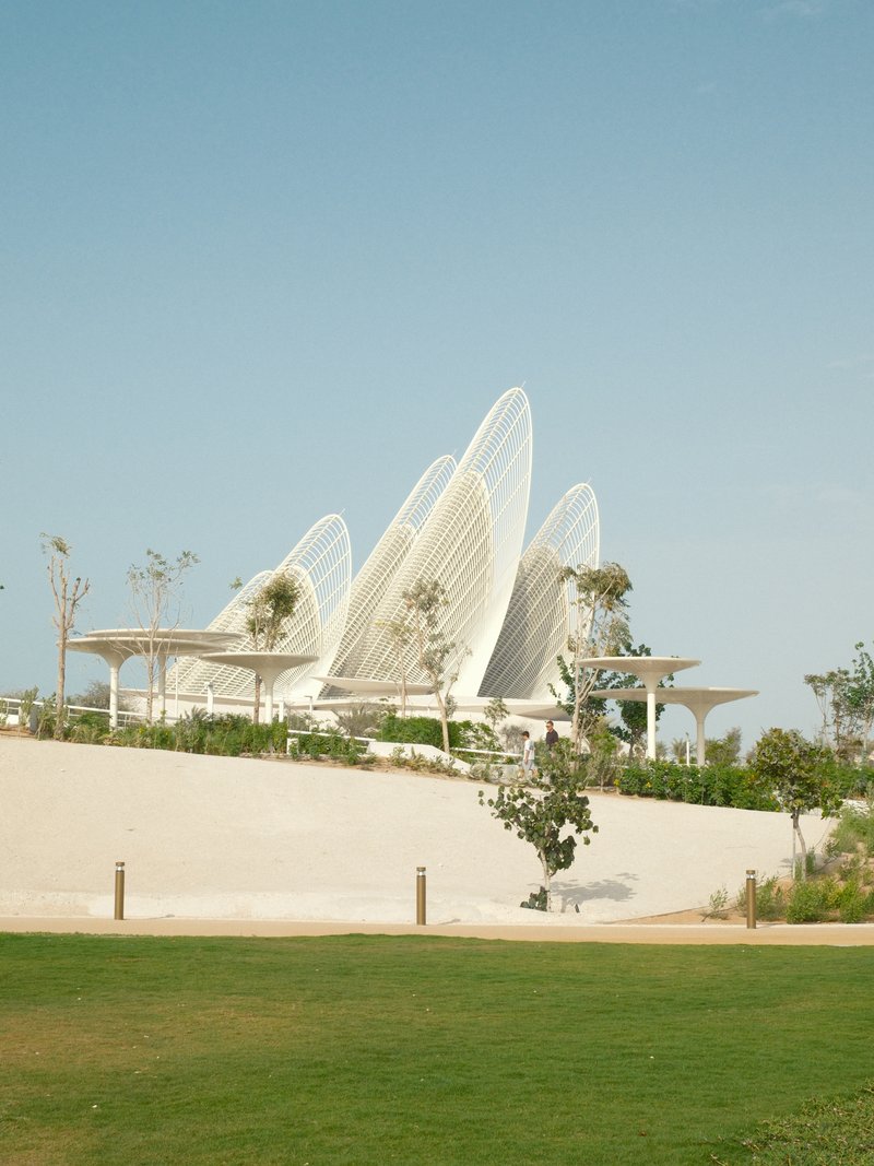 Modern architectural structure with curved white elements against a clear blue sky and green grass.