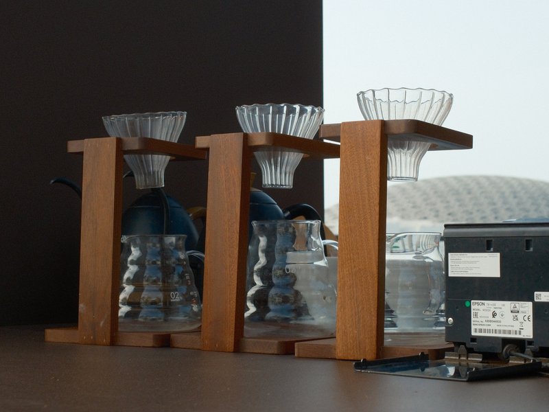 Three glass coffee drippers on a wooden stand against a blurred background.