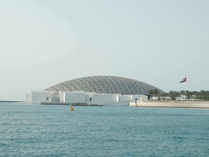 A modern architectural dome structure by the water, with a clear sky and calm sea.
