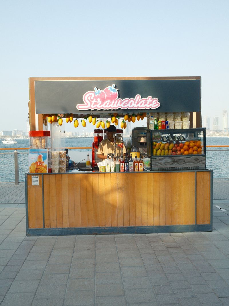 A colorful fruit juice stand by the water with a wooden structure and various fruits displayed.