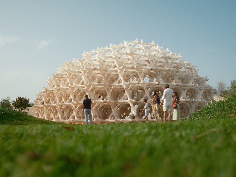 A unique architectural structure made of interlocking wooden elements with people gathered around it.