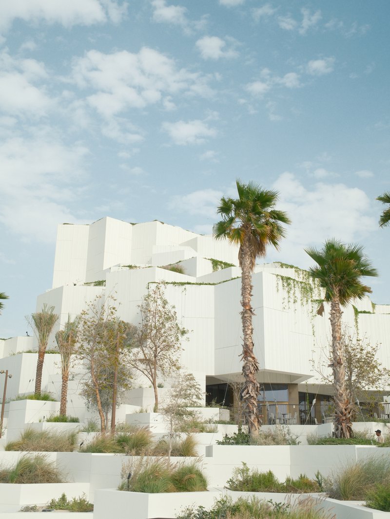 Modern white architecture with palm trees against a blue sky with scattered clouds.