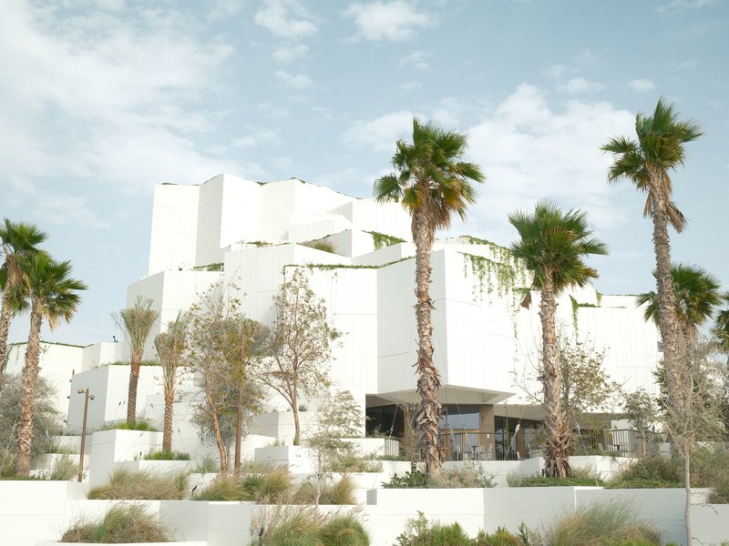 Modern white building surrounded by palm trees under a cloudy sky.