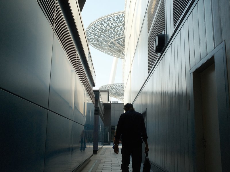 Silhouette of a person walking through a narrow alley with modern architecture and a futuristic structure above.