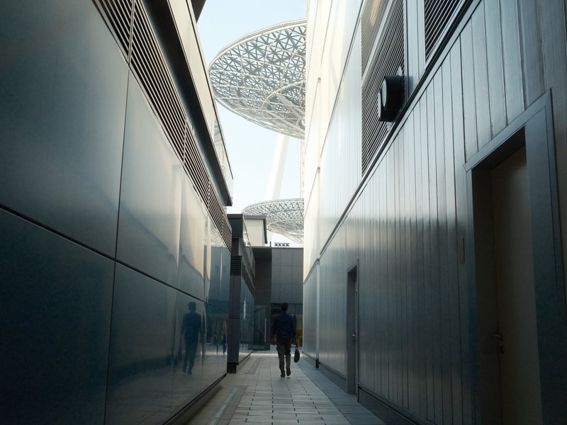 A narrow alleyway with reflective walls leading to a modern architectural structure above.