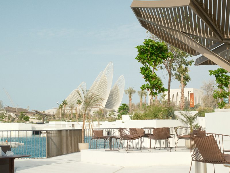 Modern architecture with curved structures in the background, surrounded by greenery and a pool area.