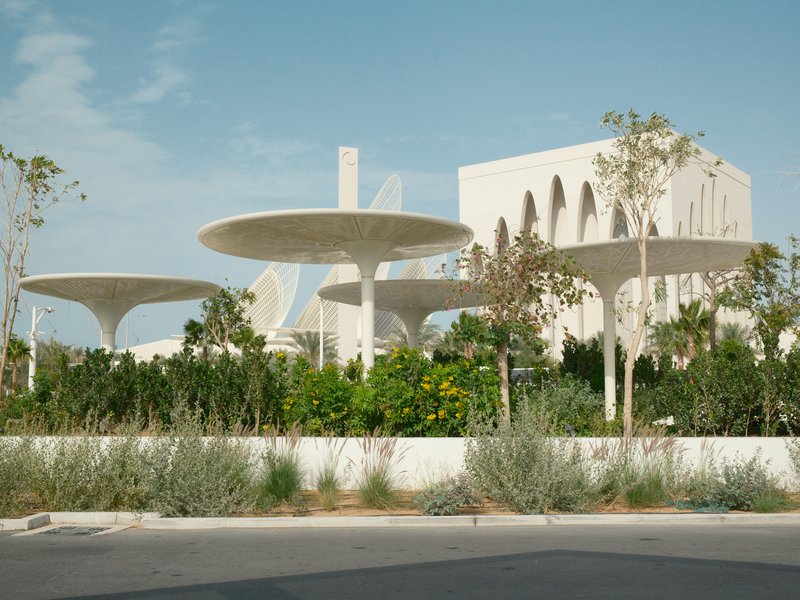 Modern architectural structure with large, circular canopies surrounded by greenery under a clear sky.