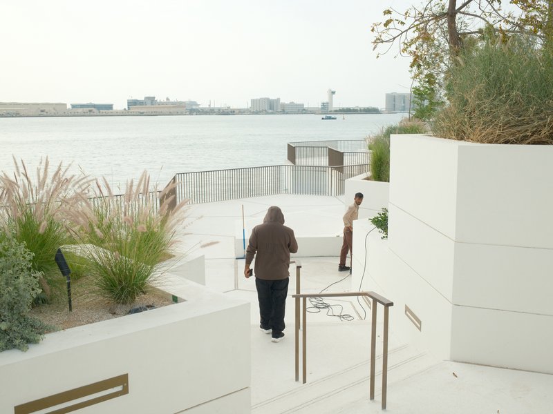 Two individuals working on a white staircase near a waterfront with buildings in the background.