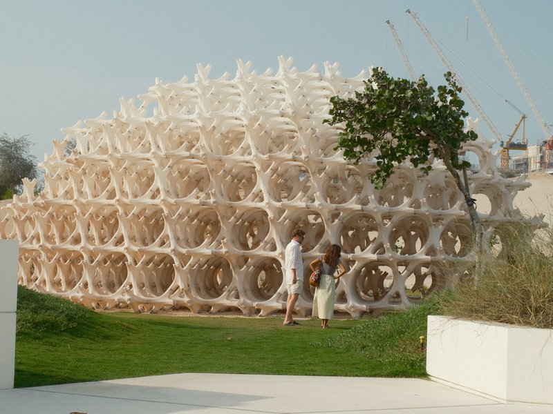 Two people walking near a large, intricate architectural structure surrounded by greenery.
