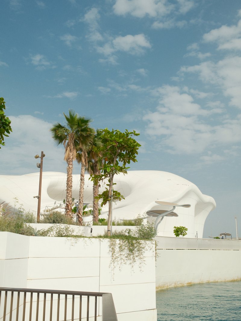 Modern white architectural structure with palm trees against a blue sky with scattered clouds.