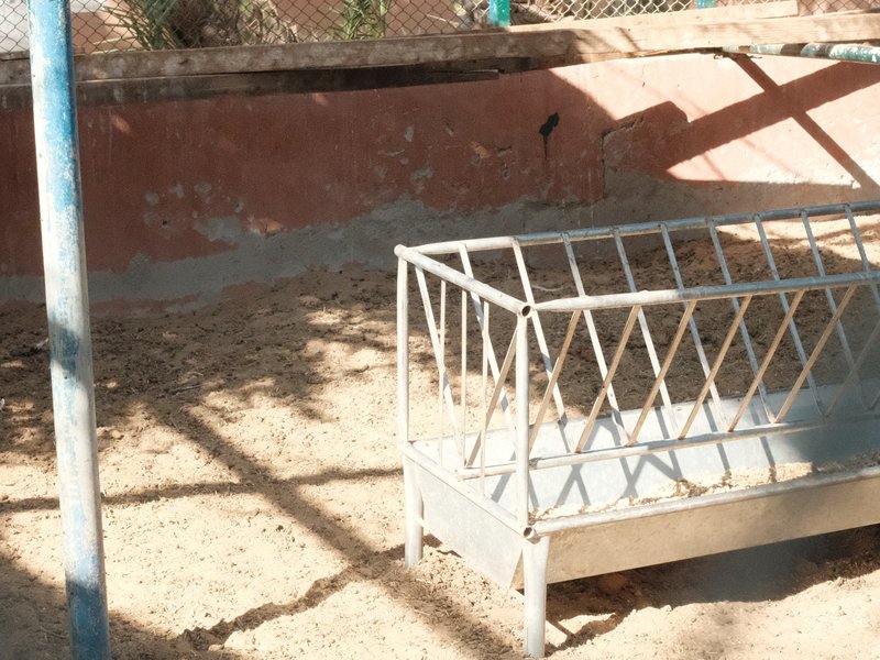 A metal structure in a dry, sunlit area with shadows cast on the ground.