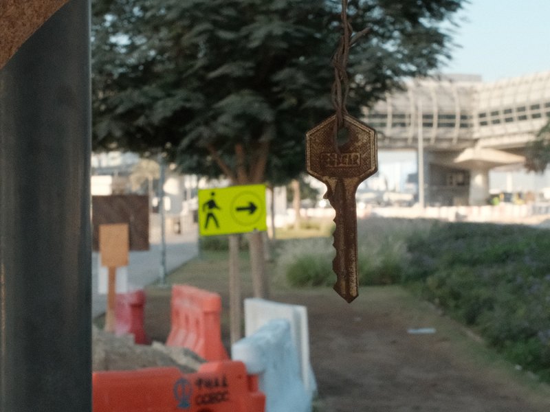 A close-up of a key hanging in focus, with a blurred urban construction scene in the background.