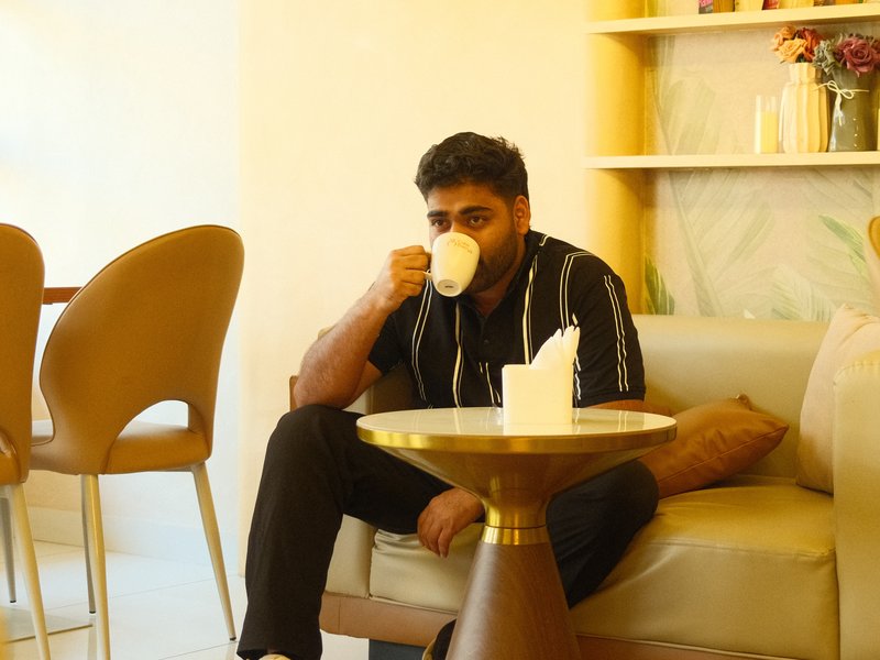 A man sitting on a sofa, sipping coffee in a cozy indoor setting with soft lighting.