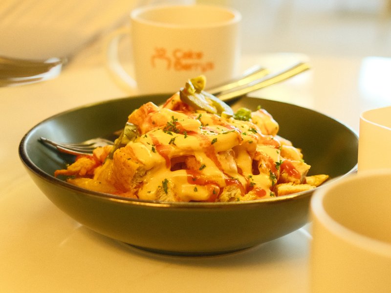 A close-up of a bowl of noodles garnished with herbs and spices, with cups in the background.