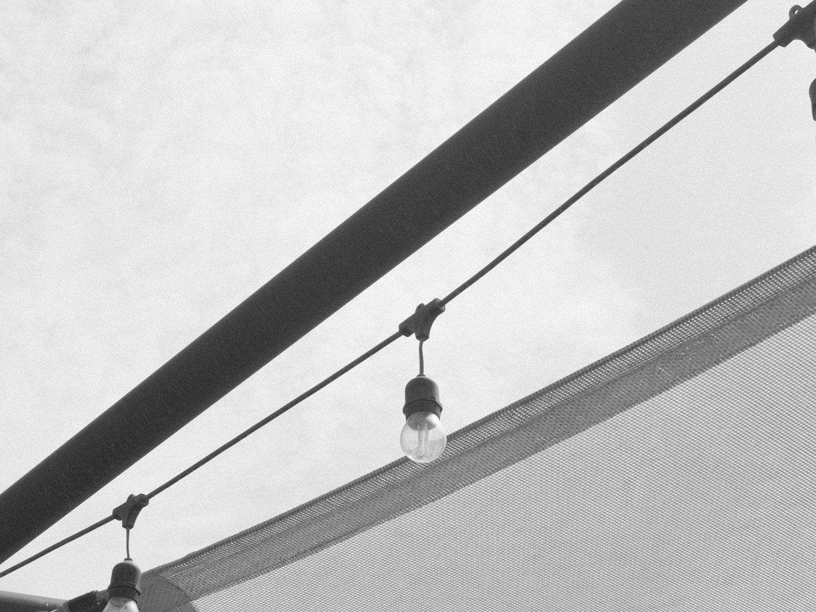 A close-up view of string lights hanging under a canopy, with a cloudy sky in the background.