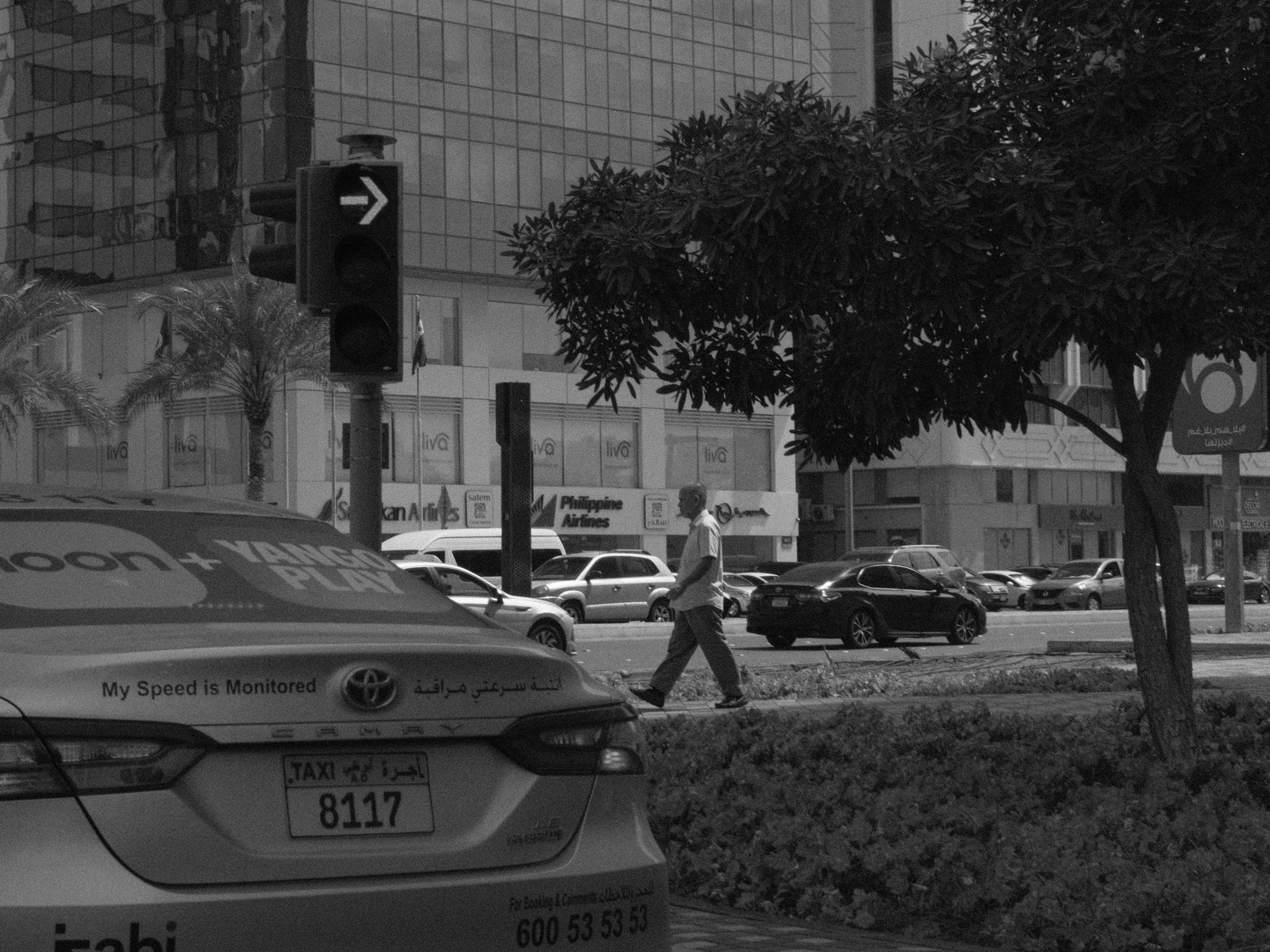 A busy street with a taxi in the foreground and pedestrians crossing, in gritty black and white