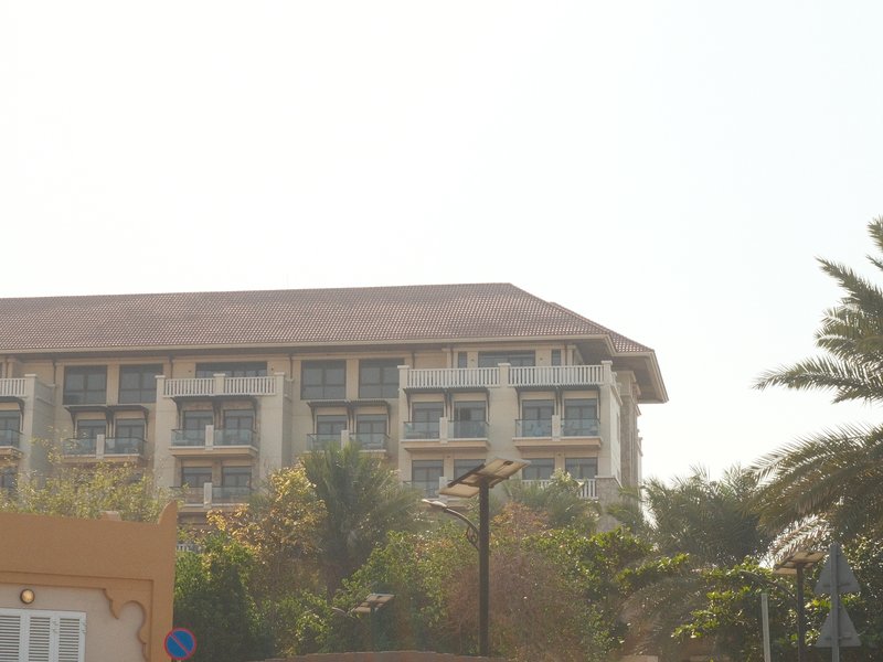 A hotel building partially obscured by palm trees under a bright sky.