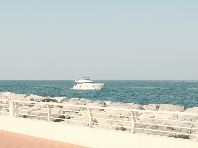 A white yacht sailing on calm blue waters near a rocky shoreline under a clear sky.