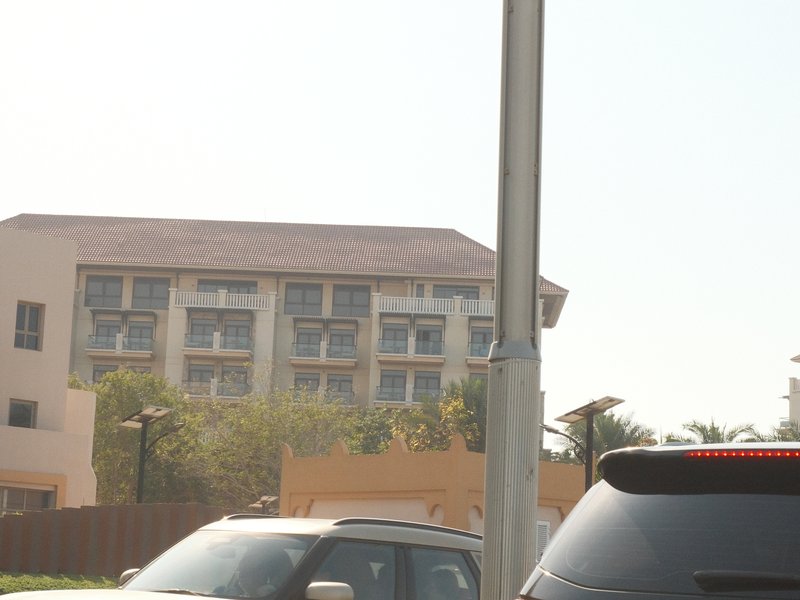 A view of a hotel building with multiple windows, partially obscured by a pole and parked cars in the foreground.