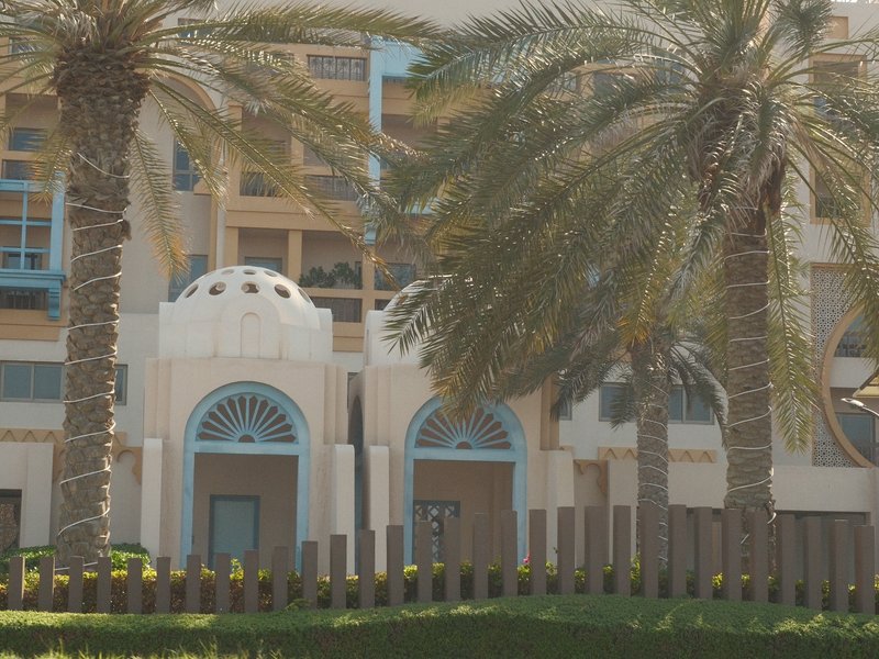 Palm trees in front of a modern building with domed architecture and blue accents.