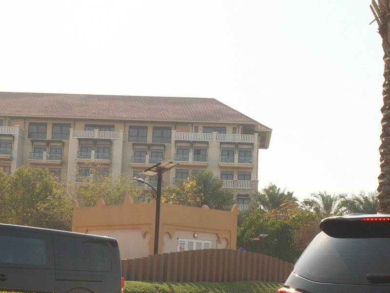 A multi-story building with a flat roof, surrounded by palm trees and a clear sky.