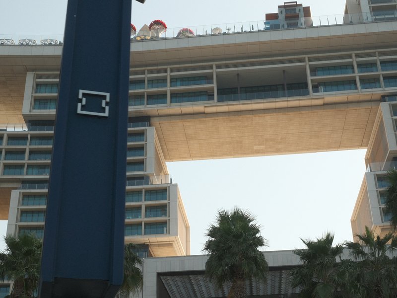 View of a modern architectural structure with a large opening, framed by palm trees and a blue vertical element.