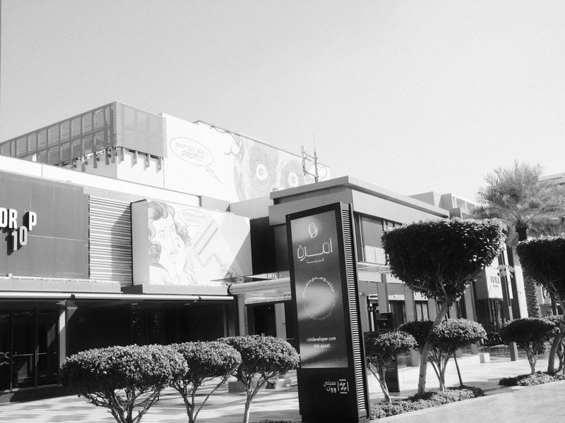 A modern building facade with neatly trimmed hedges and a sign in a sunny urban setting.