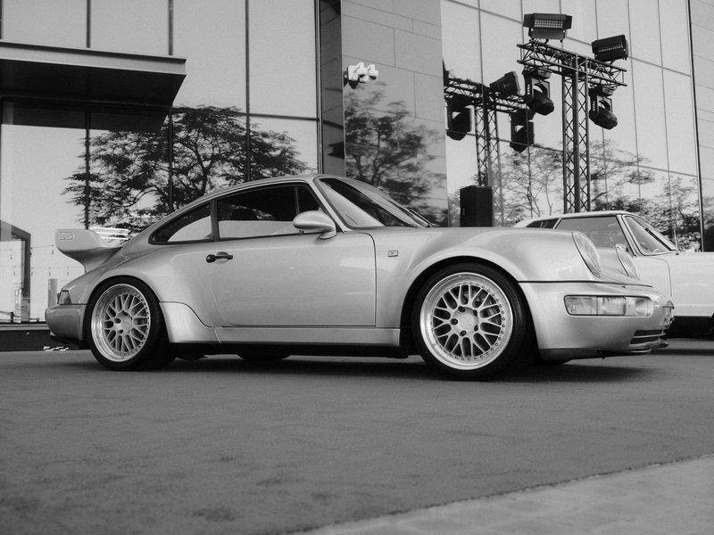 A silver sports car parked in front of a modern building with reflections and stage lights.