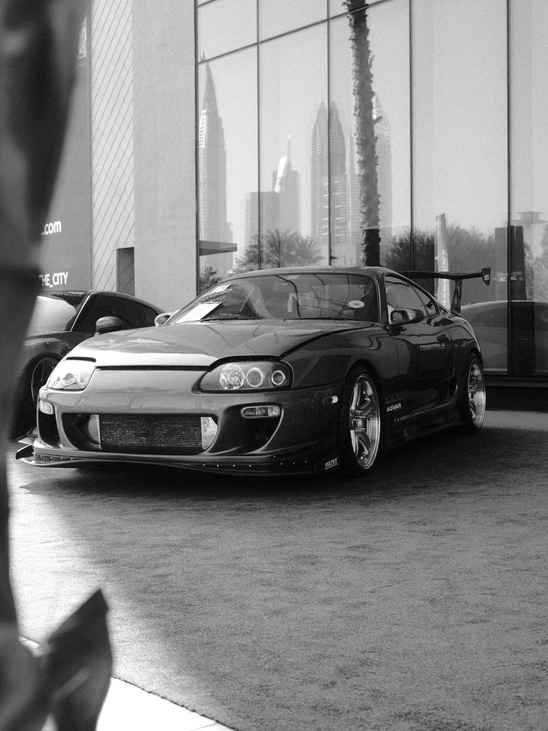 A sleek black sports car parked in front of a modern building with city skyline in the background.