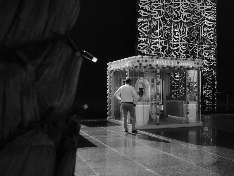 A man walking towards a glass structure with intricate designs in a dimly lit environment.