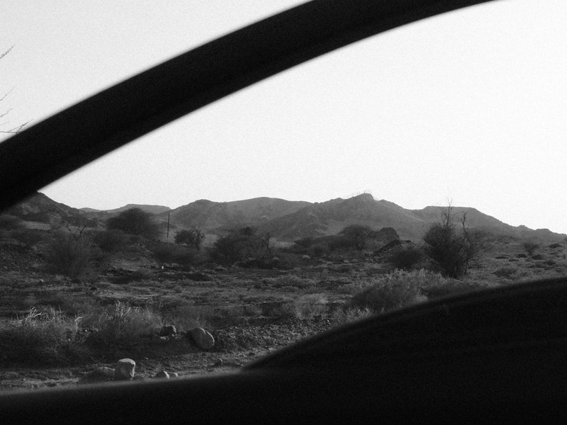 Black and white photo of mountains viewed through a car window, with a focus on the landscape outside.