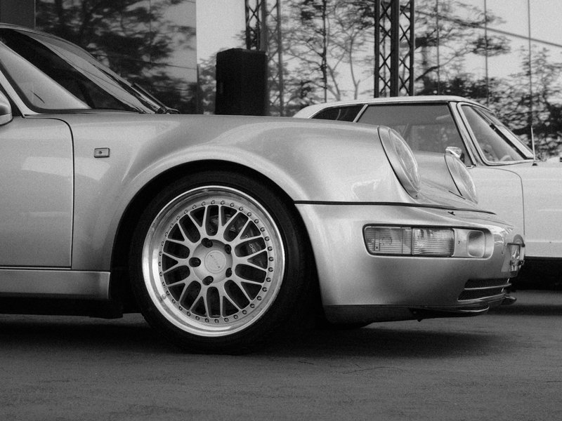 Close-up of a silver sports car with detailed alloy wheels, set against a blurred background of another car.