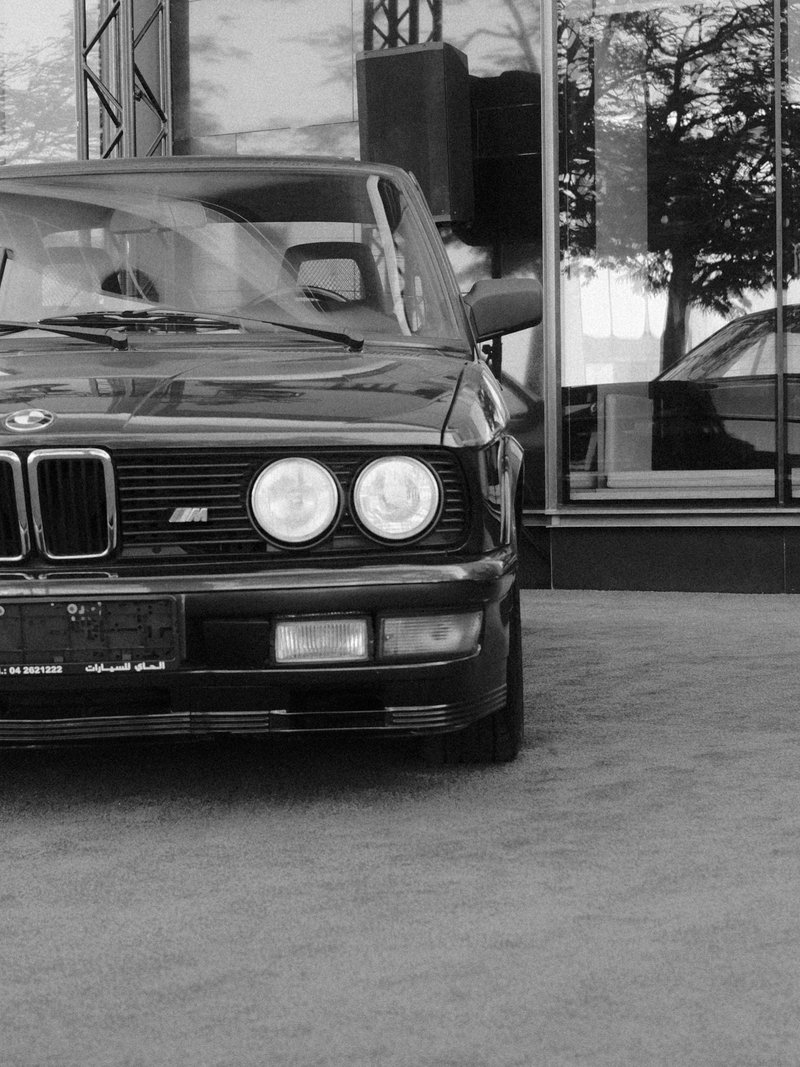 A classic black BMW car parked in front of a reflective glass building.