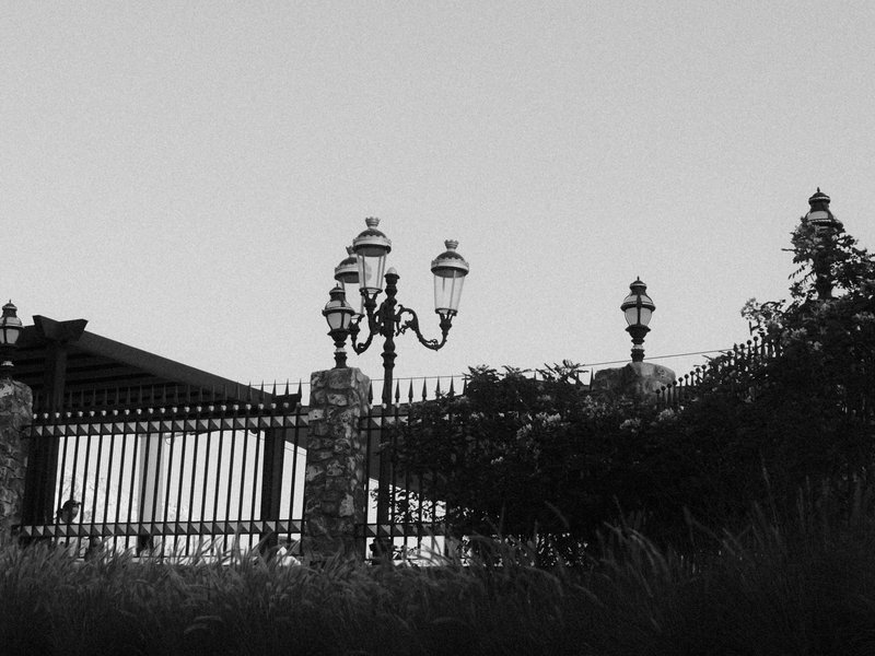 A vintage-style lamppost stands near a wrought iron fence against a clear sky.