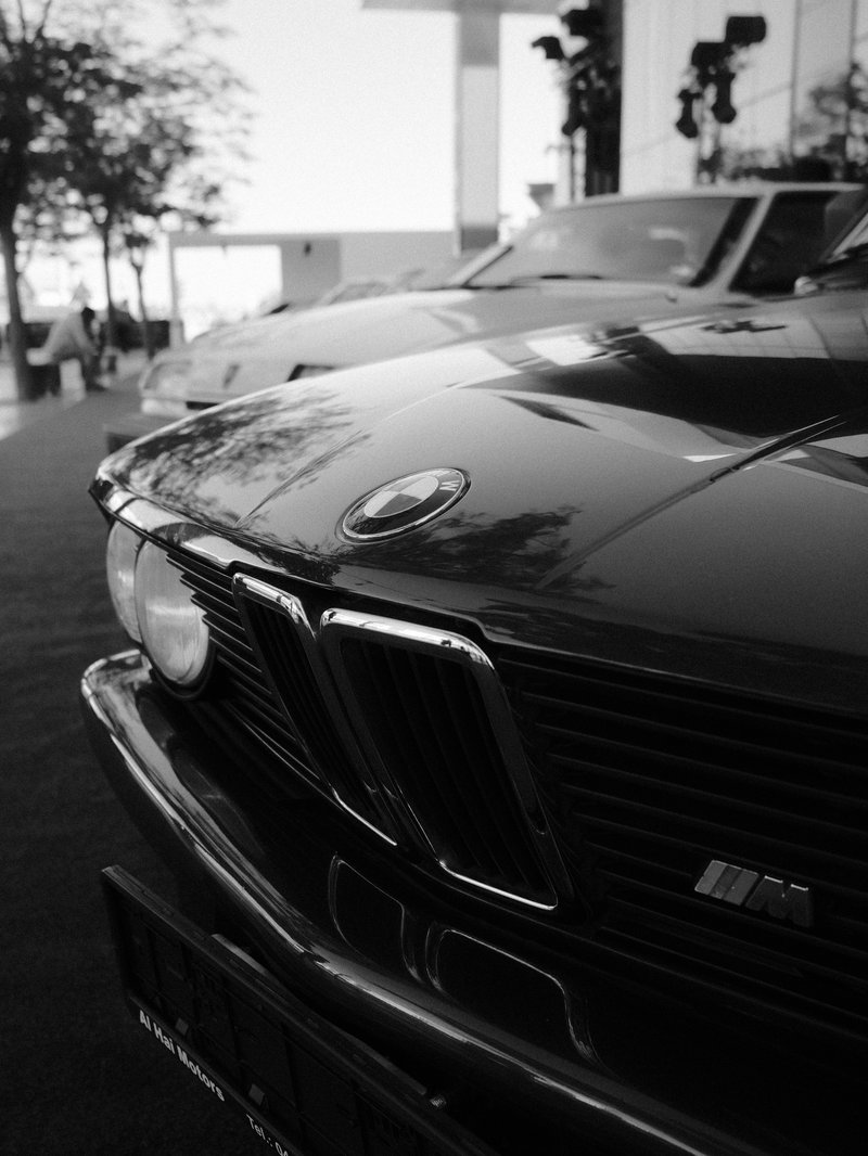 Close-up of a classic black car's front grille with blurred vintage cars in the background.