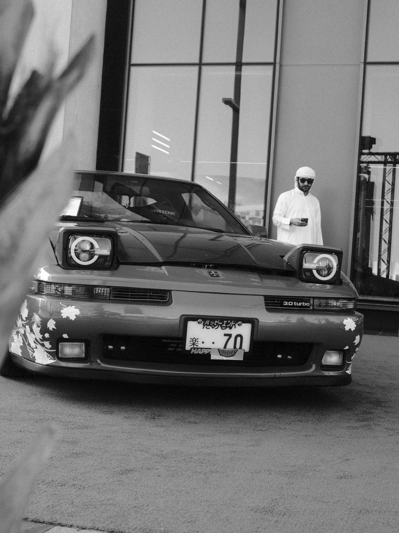 A vintage car with floral decals parked in front of a modern building, with a person in white attire standing nearby.