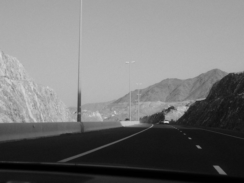 A winding road with mountains in the background, captured from inside a vehicle.