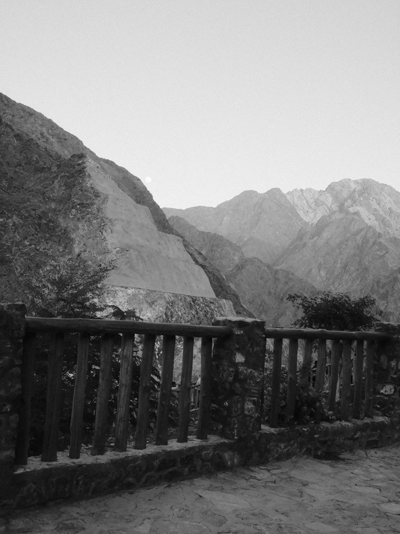 Black and white photo of a mountain landscape with a stone railing in the foreground.