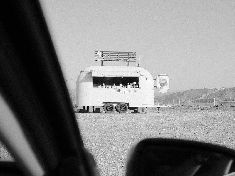 A food truck parked in a desolate landscape, viewed from inside a car.
