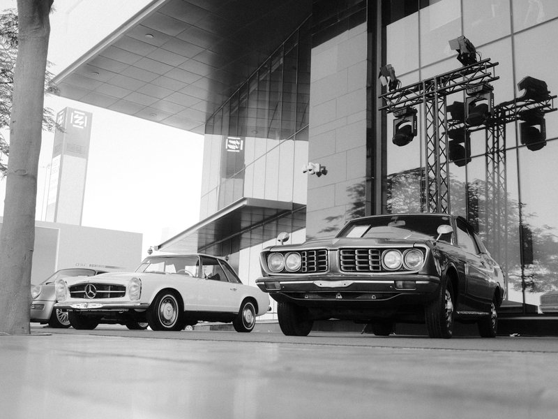 Two classic cars parked in front of a modern building with large glass windows.