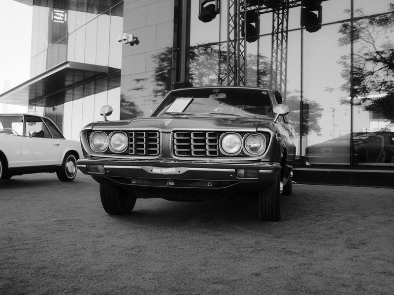 Classic car parked in front of a modern glass building, showcasing a blend of old and new architecture.