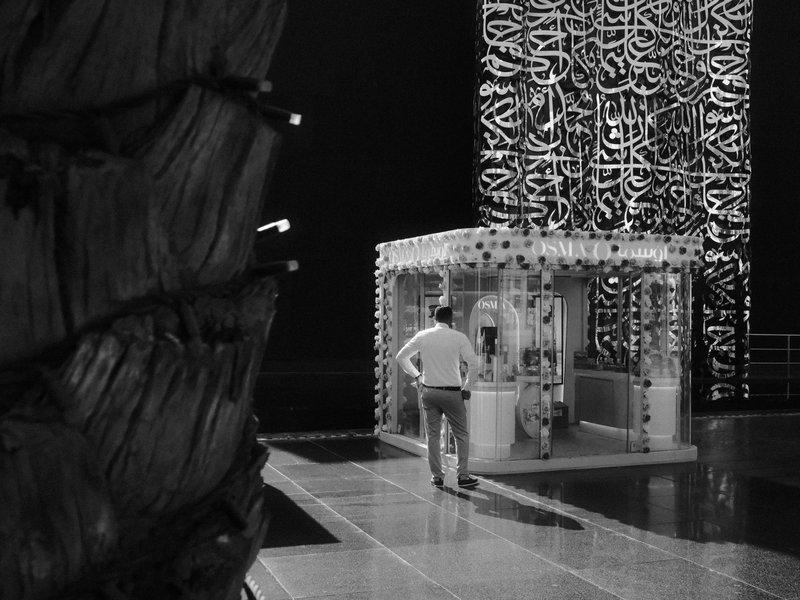 A man stands near a transparent structure with intricate patterns, surrounded by dark shadows.