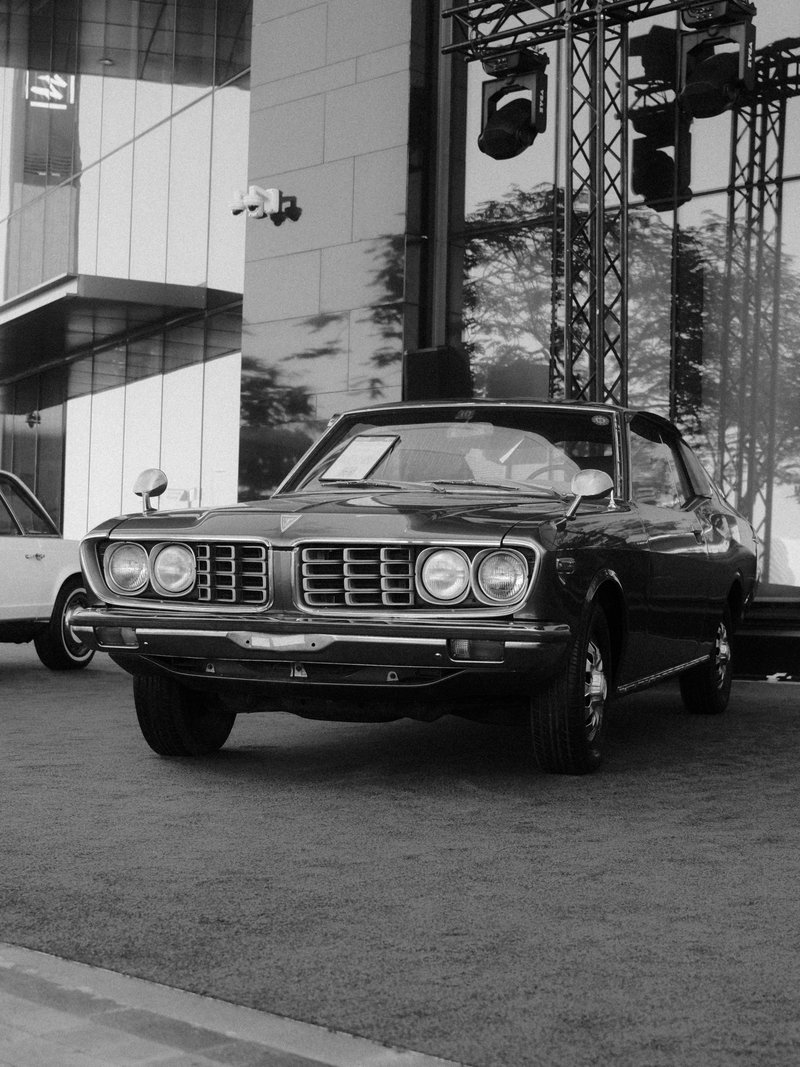 A classic black car parked in front of a modern building with stage lights.