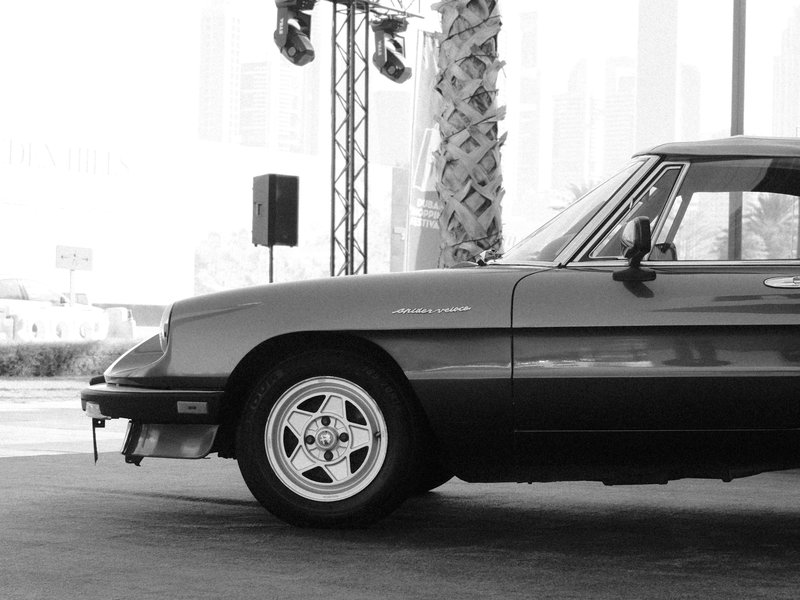 Side view of a classic car parked at an event, with palm trees and urban backdrop.