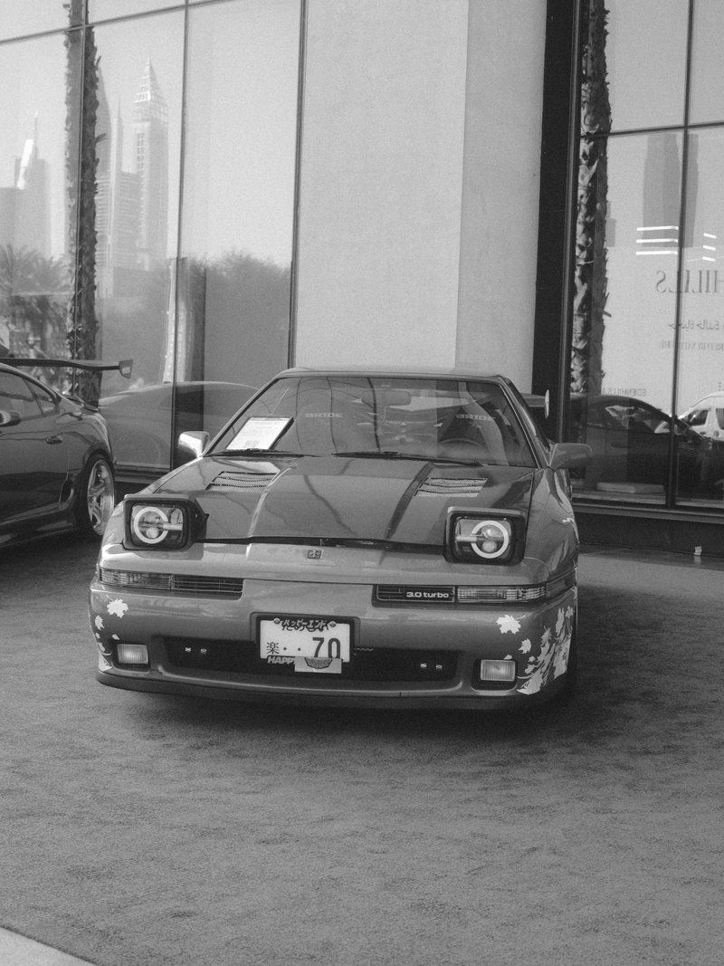 A vintage car displayed in front of a modern building, with city skyline in the background.