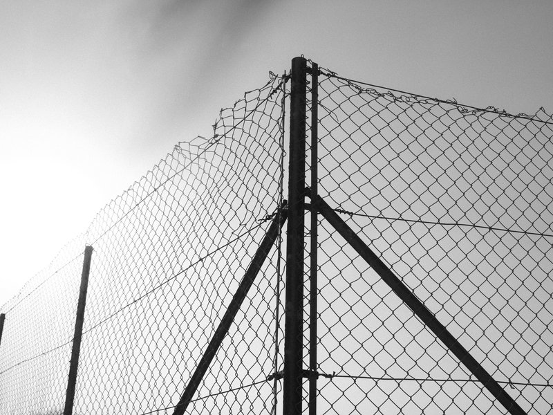 A close-up of a chain-link fence against a bright sky, capturing the texture and structure of the fence.