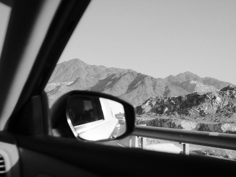View from a car window showing mountains in the distance and a side mirror reflecting part of the car.
